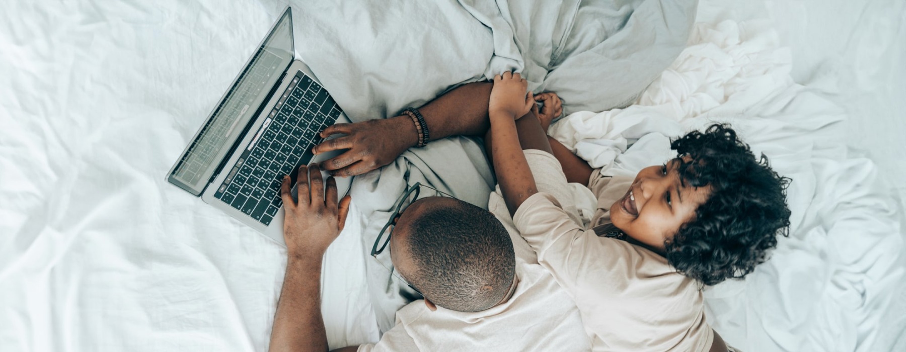 a man and his child on a bright bed while he works on a laptop