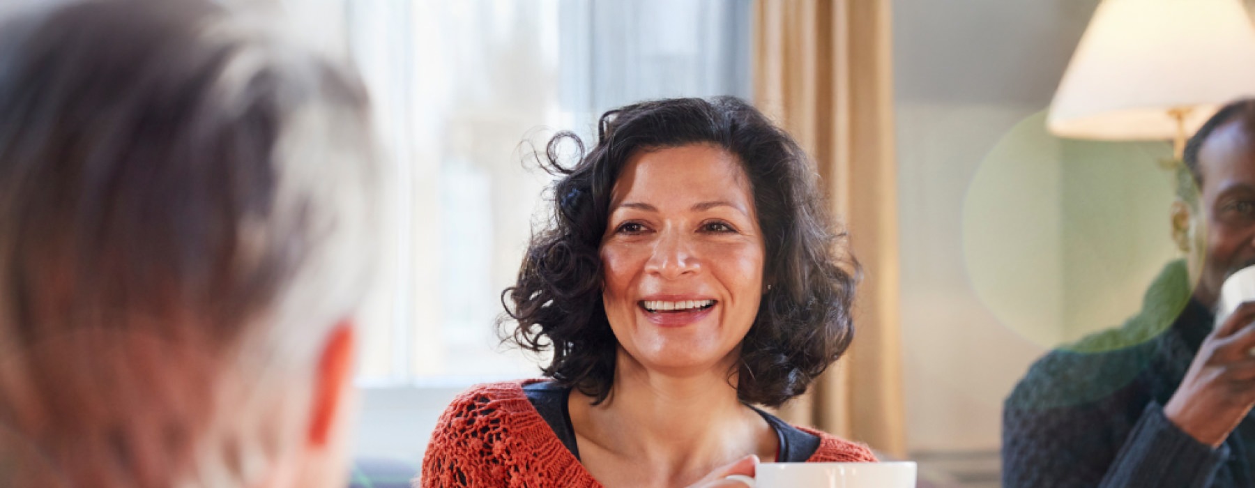 Woman holding a cup of coffee and socializing with other people in a living room