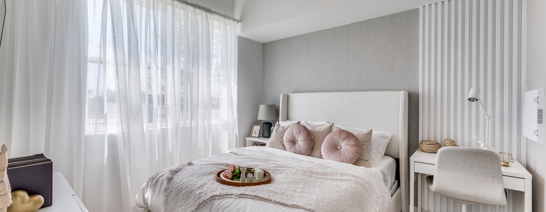 A bedroom with a large window and a white bed and a desk